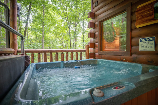 Hot tub on cabin porch with view of trees