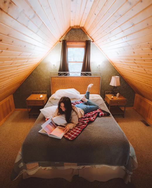 girl on bed reading in loft of cabin